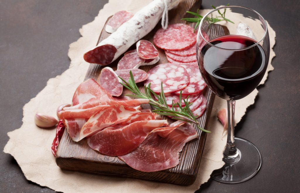 Volpi Foods Prosciutto And Wine Pairing Salami, sliced ham, sausage, prosciutto, bacon and red wine glass. Meat antipasto platter on stone table
